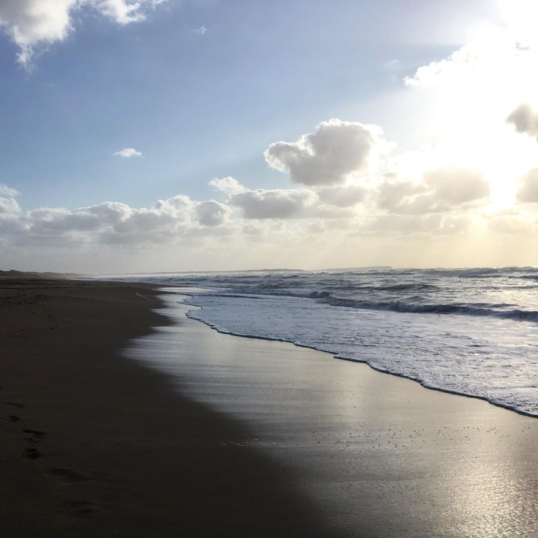 Spiaggia selvaggia davanti al campeggio Nurapolis in Sardegna, con onde che si infrangono sulla riva e il sole che illumina le nuvole